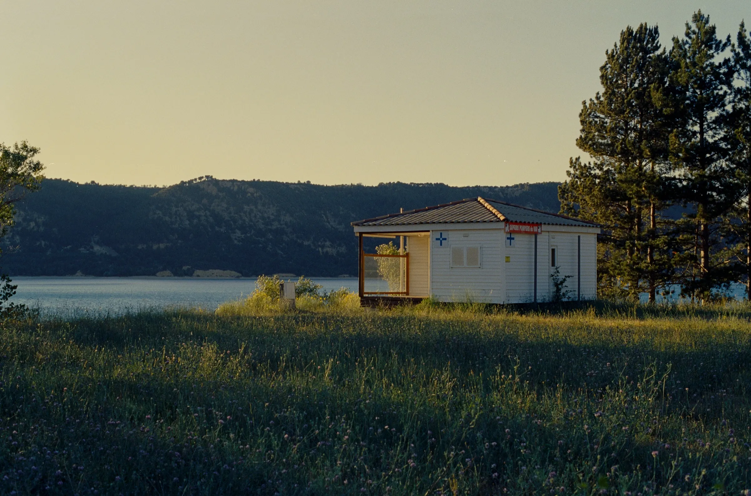 A small white cabin beside a lake at golden hour